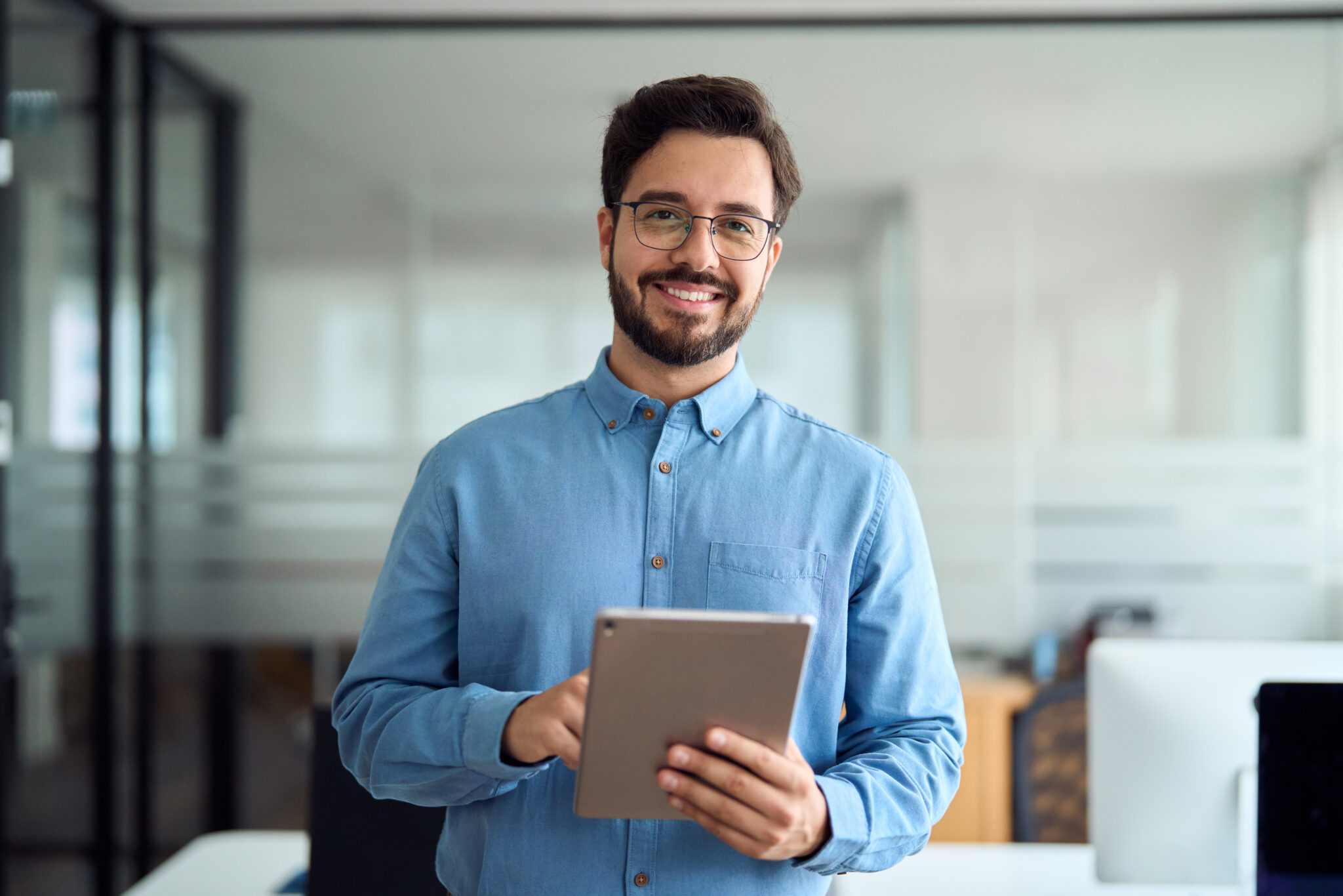 Smiling young business man manager with tab standing in office. Portrait.